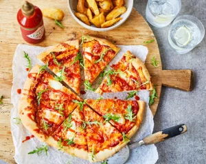 Wooden board with sliced pizza, potato fries and Tabasco Sriracha sauce