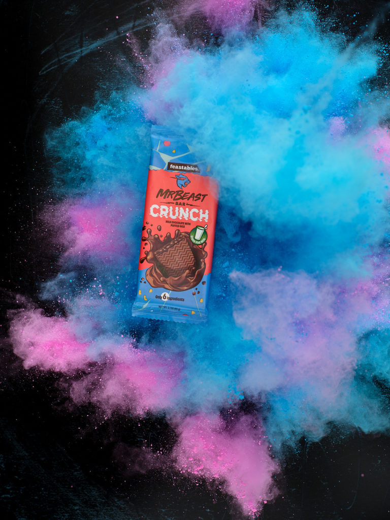 Blue and pink color explosion around Milk Crunch Chocolate bar 60 gram from Feastables by MrBeast